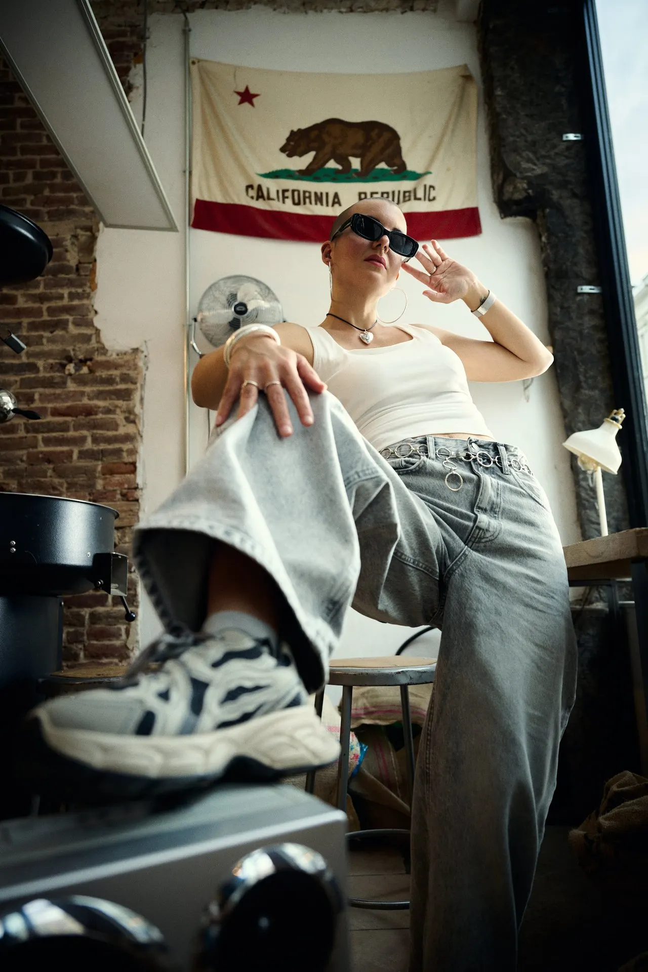 Femme en jean et top blanc devant un drapeau californien, ambiance streetwear, éditorial mode, Bruxelles