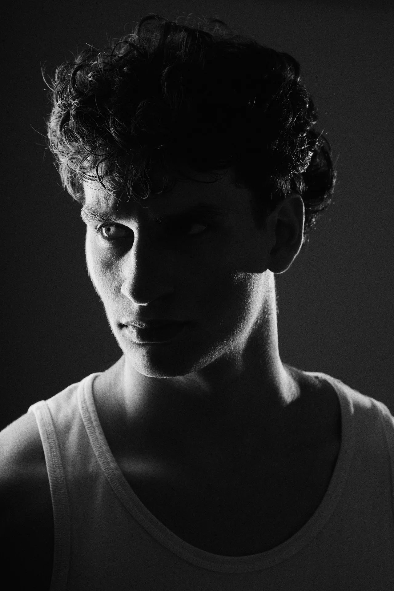Portrait noir et blanc d'un homme aux cheveux bouclés en débardeur, clair-obscur, éditorial, Bruxelles
