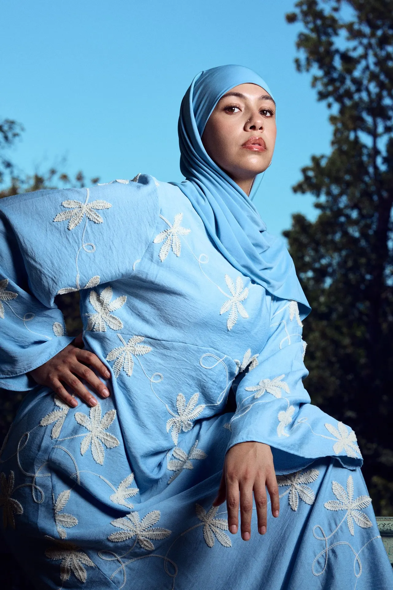 Femme en ensemble et hijab bleus à motifs floraux, en extérieur sous un ciel bleu, mode éditoriale, Bruxelles