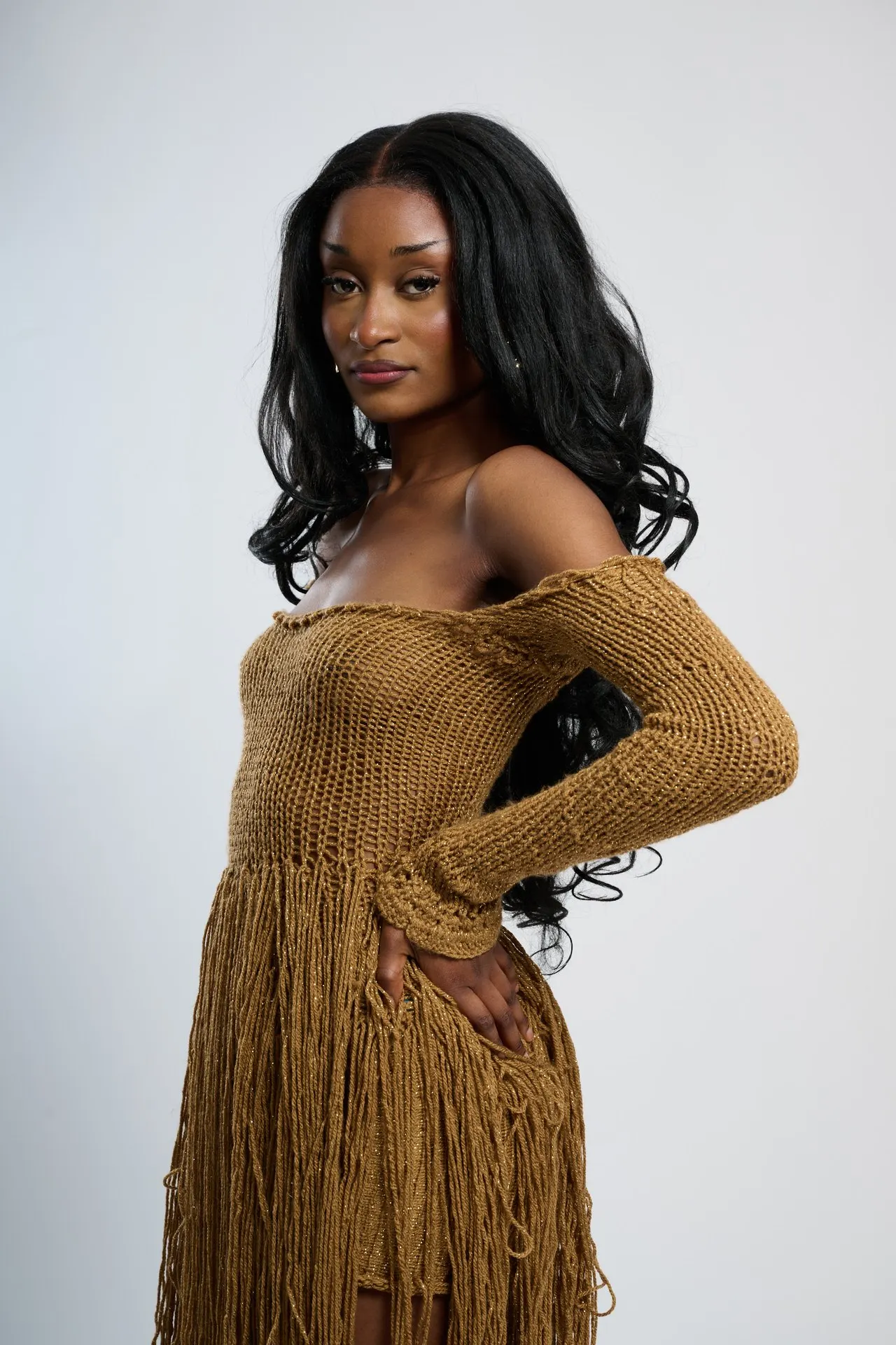 Femme en robe crochet ocre à franges, longs cheveux, studio blanc, mode éditoriale, Bruxelles