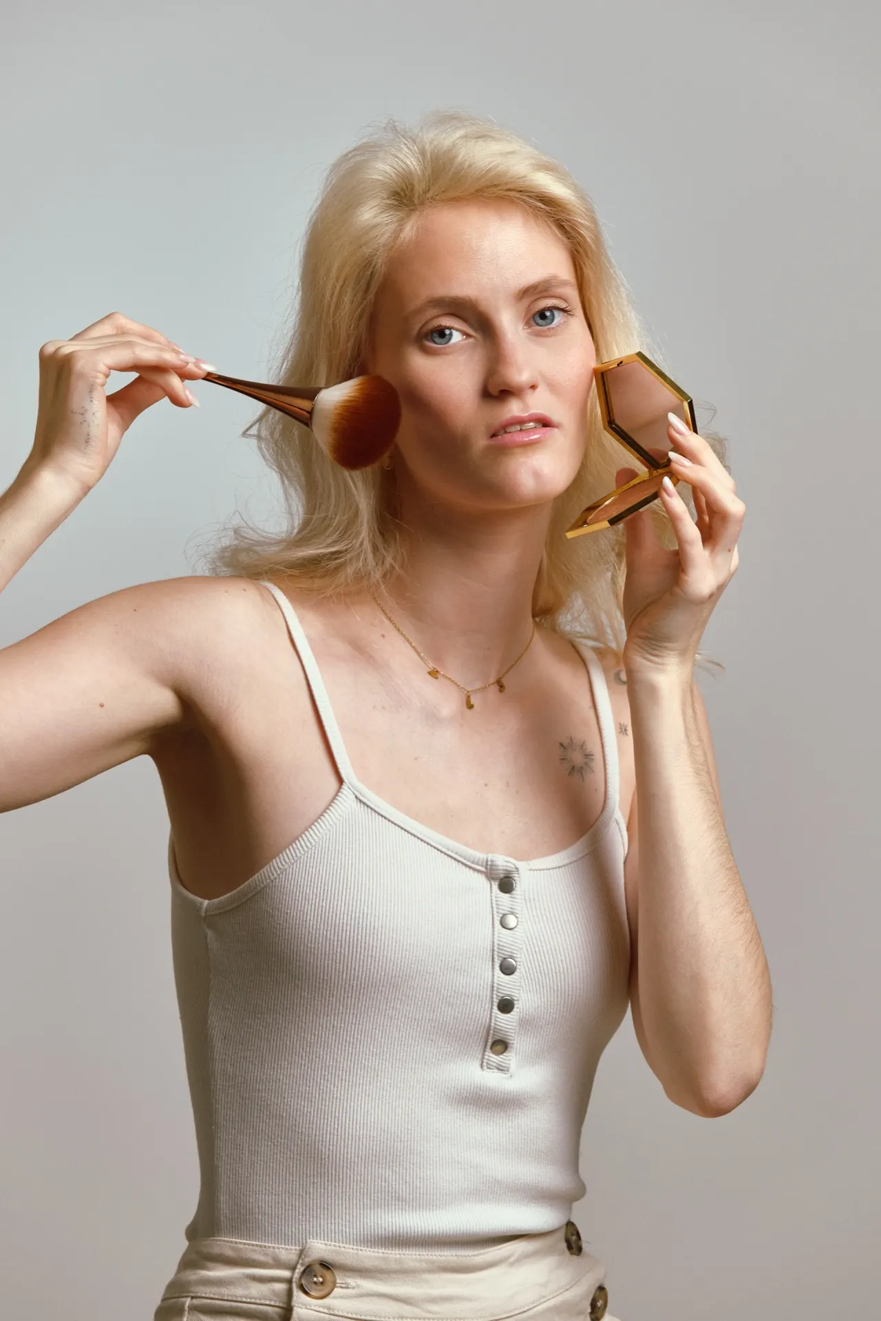 Femme blonde appliquant du fond de teint au pinceau, séance beauté studio, Bruxelles