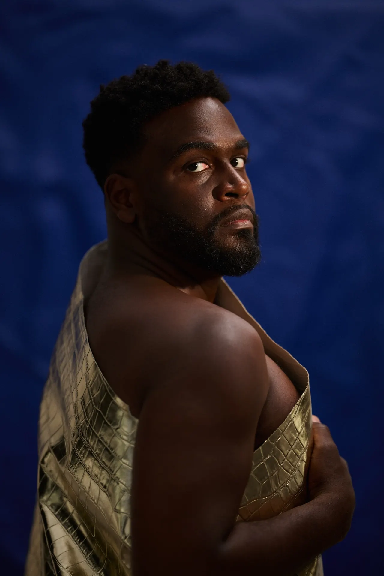 Homme torse nu drapé d'un tissu doré sur fond bleu, portrait studio, Bruxelles