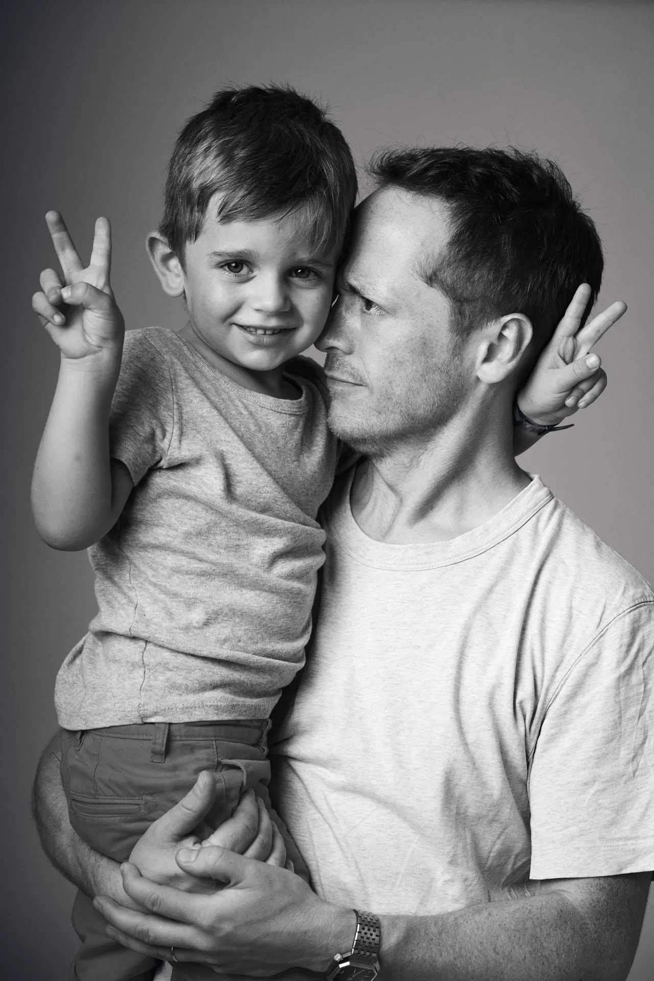 Père et son jeune fils en noir et blanc faisant le signe de paix, séance famille en studio, Bruxelles