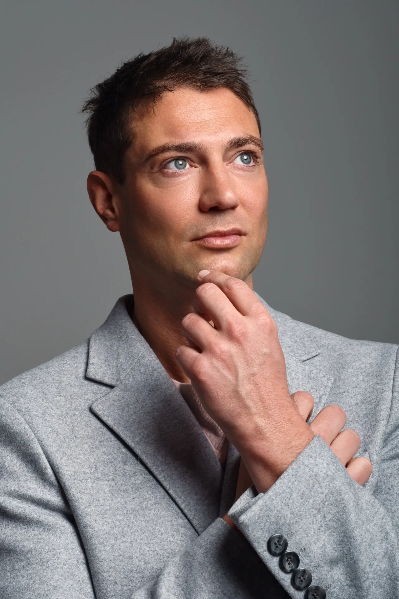 Homme en veste grise, main au menton, regard pensif, portrait studio, Bruxelles